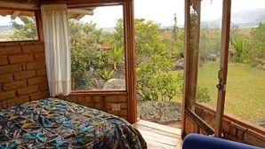 A room with a bed, a window, and a view of a garden. - Mawasi Finca (Villa de Leyva)