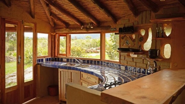 A kitchen with a curved blue-tiled countertop, wooden cabinets, and a view of greenery outside. - Mawasi Finca (Villa de Leyva)