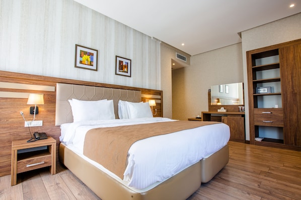 A hotel room with a large bed, wooden headboard, bedside tables, a wardrobe, and a mirror.