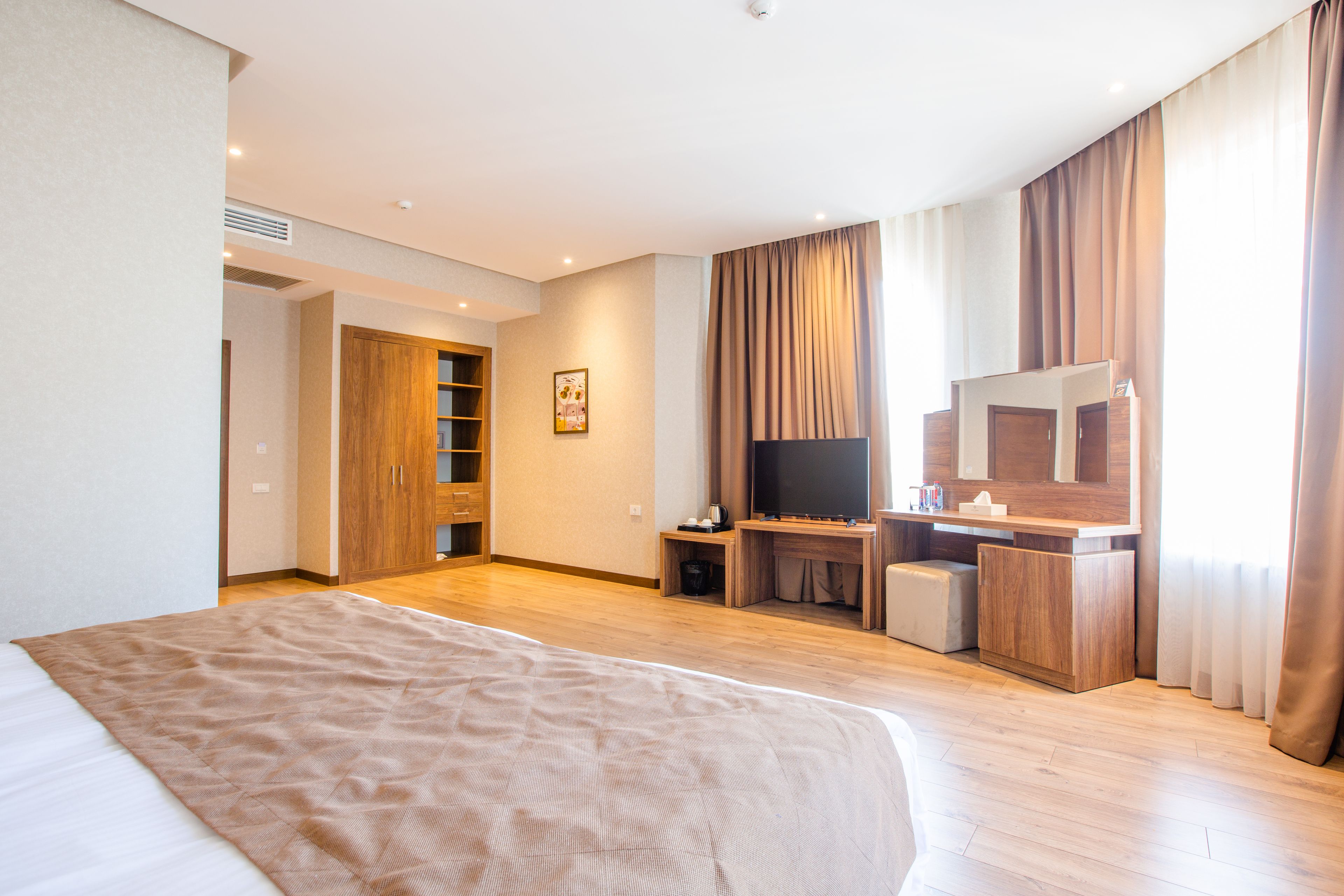 A modern hotel room with a large bed, wooden flooring, a TV, a desk, and a wardrobe.
