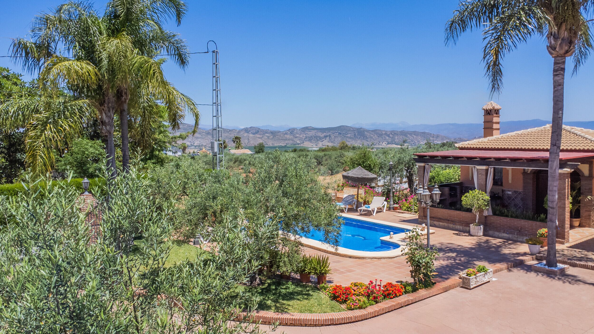 Zona de piscina amb vistes a les muntanyes, envoltada de vegetació i un porxo.