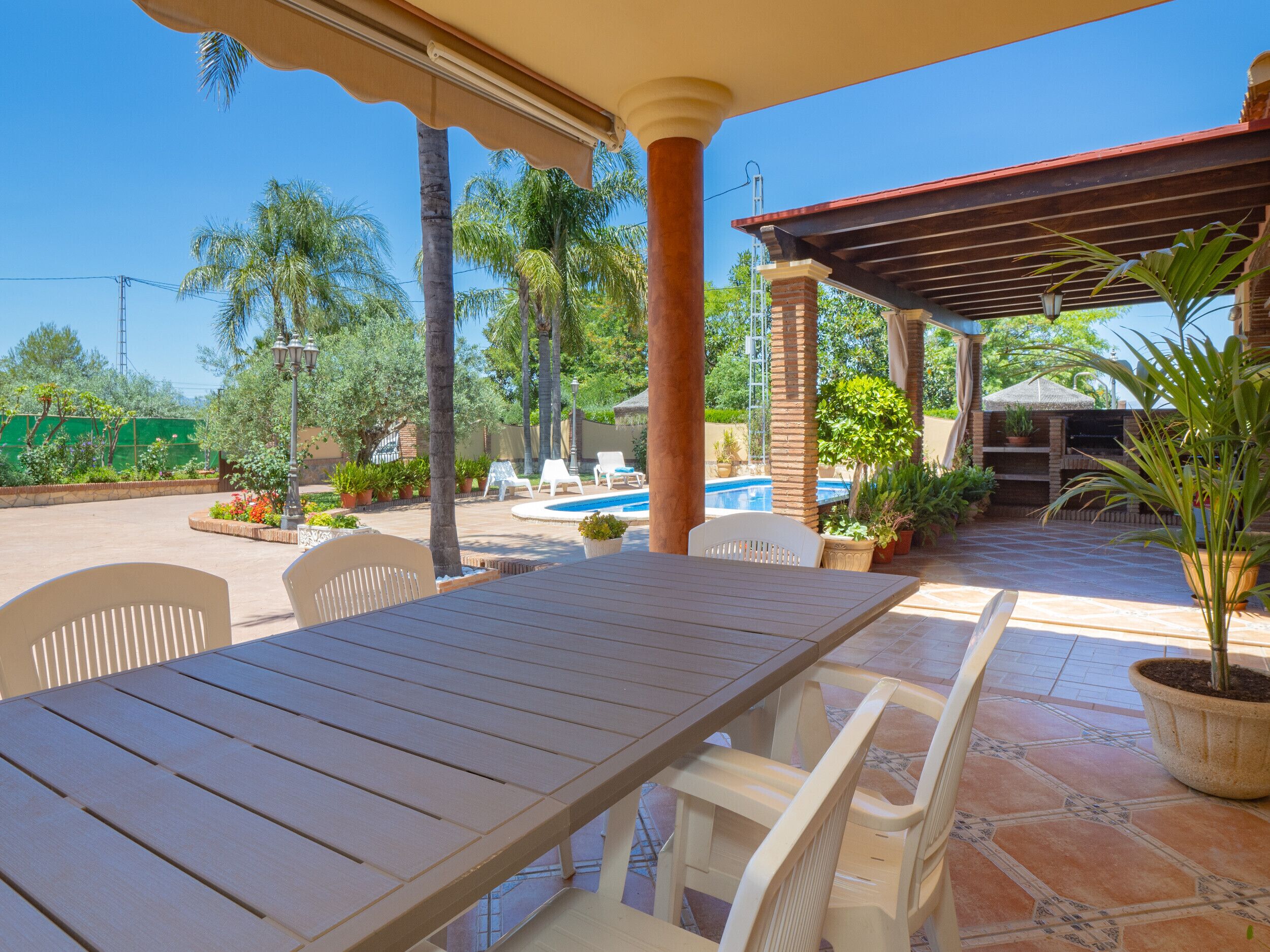 An outdoor patio with a pool, white chairs, and a table.