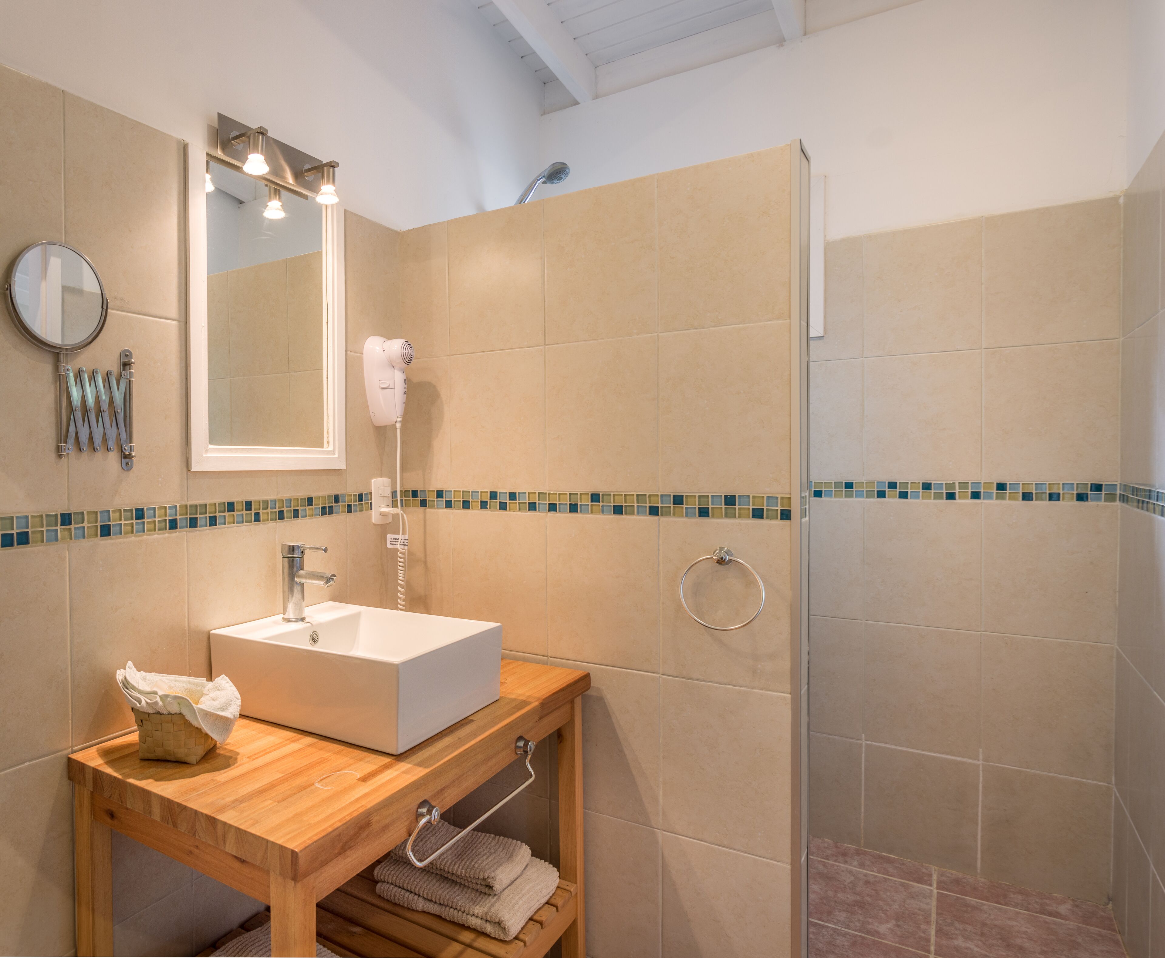 A bathroom with a wooden vanity, a sink, a mirror, a hairdryer, and a shower area.