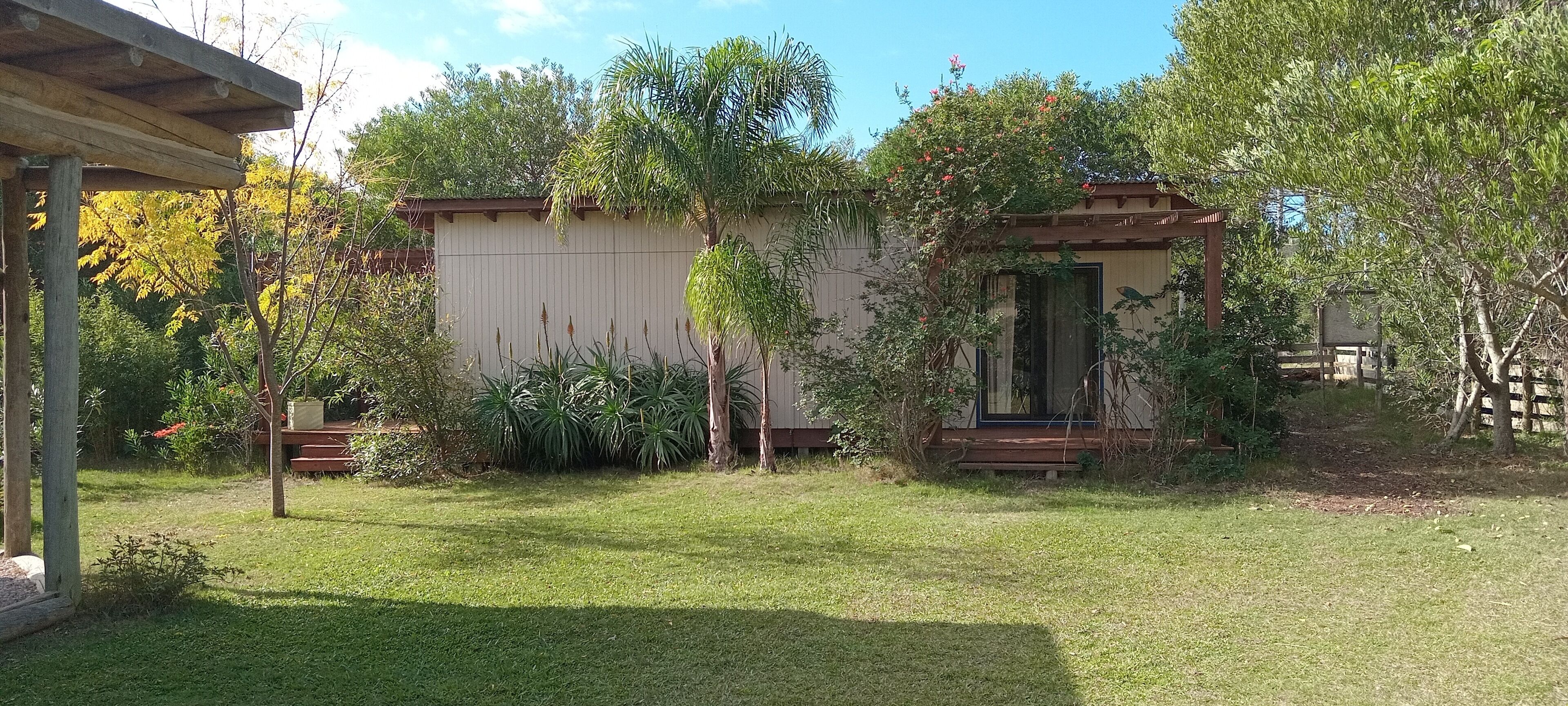 A small, single-story building with a covered porch, surrounded by a well-maintained lawn and various plants.