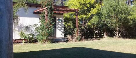 Um jardim com pérgola, um pequeno galinheiro e diversas árvores e arbustos.