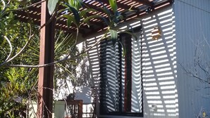 Un espace extérieur abrité, doté d’une pergola en bois, d’une petite table et d’un escalier menant à une porte.