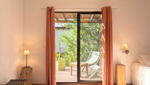 Une chambre dotée d’une grande porte-fenêtre coulissante donnant sur une terrasse extérieure avec une chaise et une table.