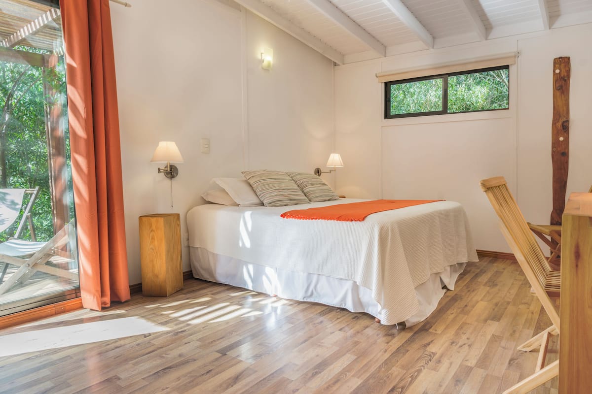 Ein Schlafzimmer mit einem Bett, einem Fenster, einem Holzboden und einem Sessel.