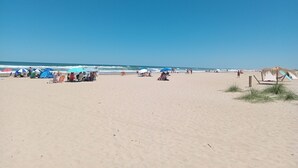 Une plage avec des parasols, des chaises longues et une structure recouverte de chaume.