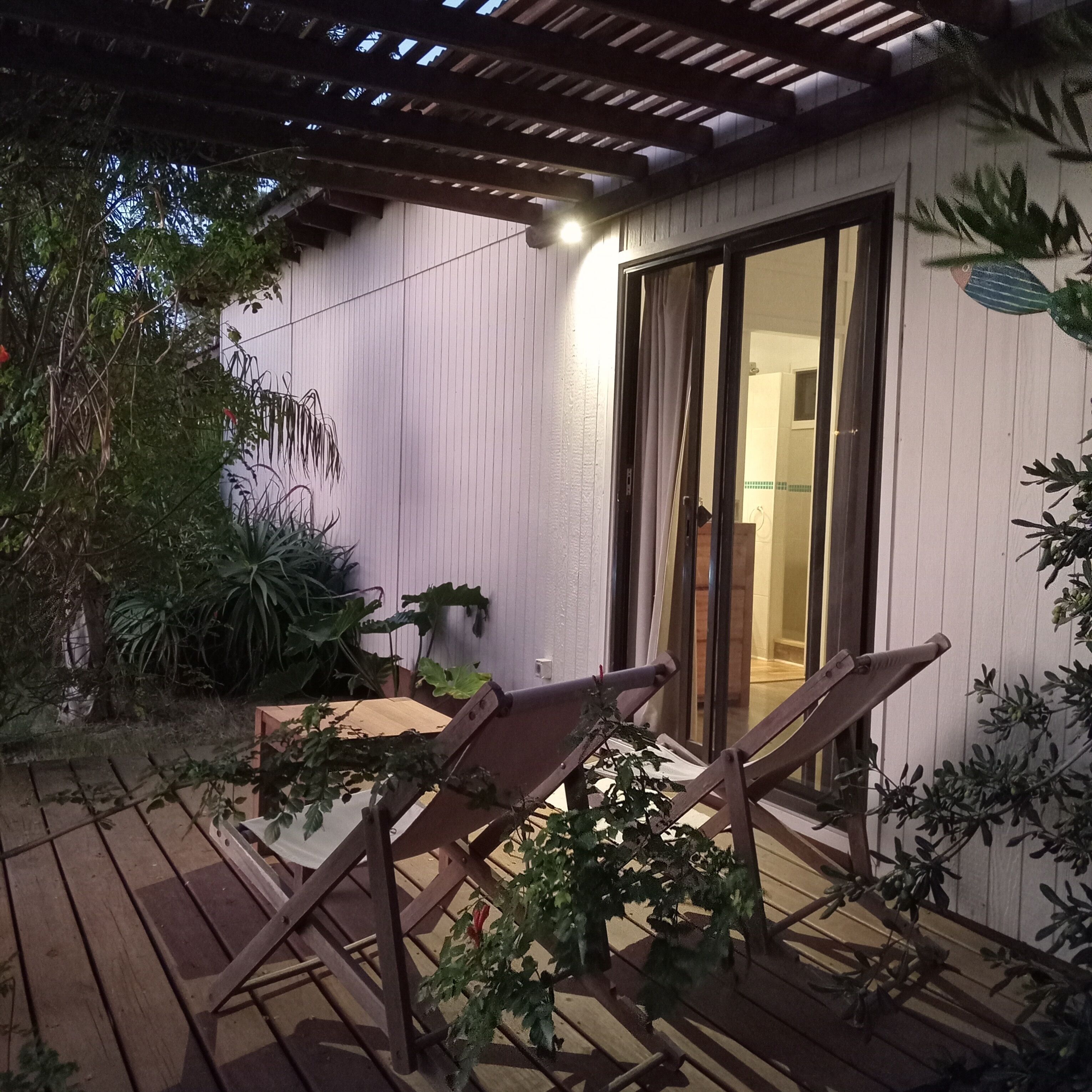 An outdoor patio with wooden flooring, a table, two chairs, and potted plants.