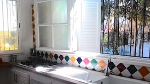 Eine Küche mit weißer Arbeitsplatte, einem Spülbecken und einem Fenster mit farbenfroher, diamantmusteriger Spritzschutzleiste.