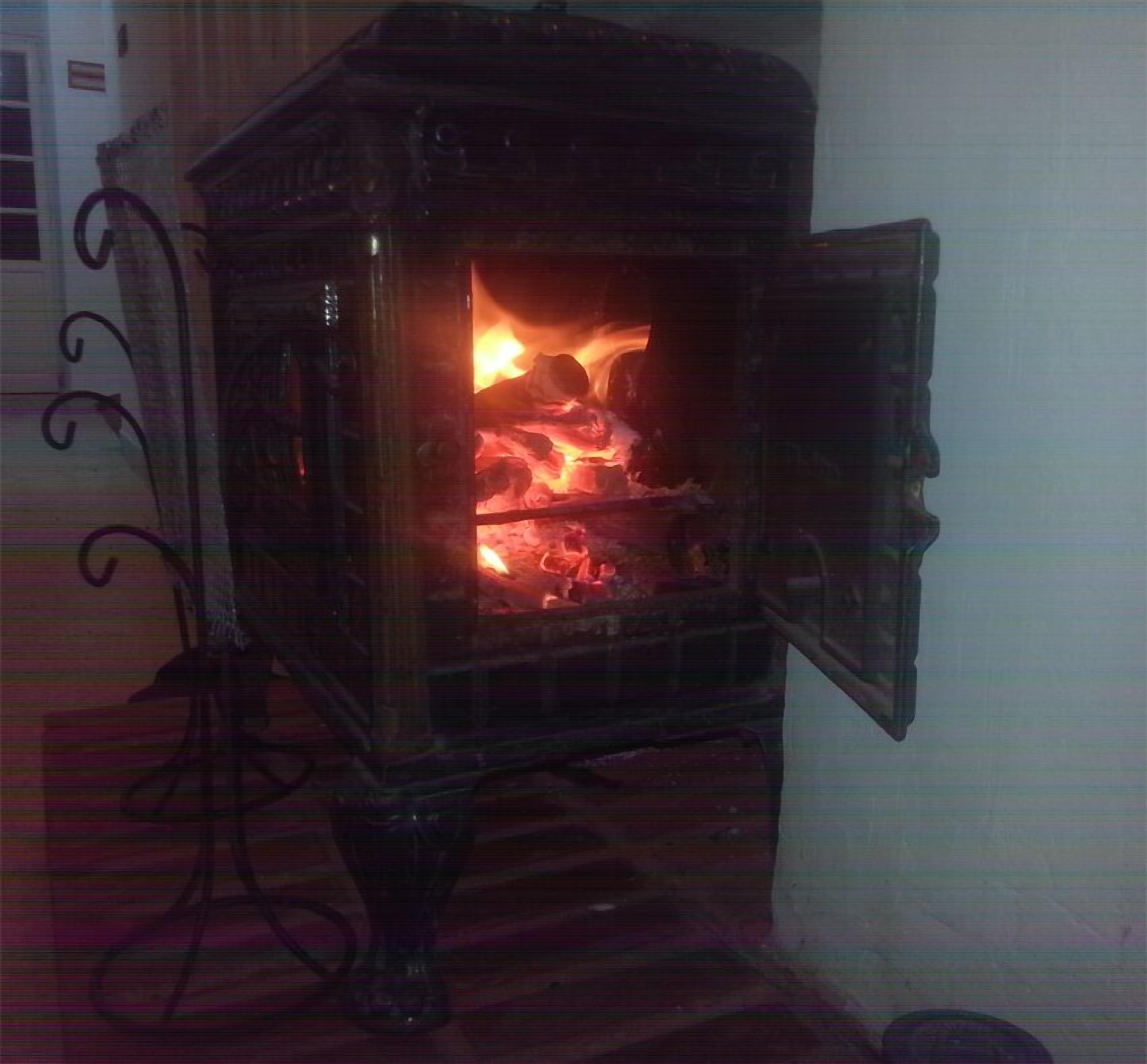 A wood-burning stove with an open door, revealing a fire inside.