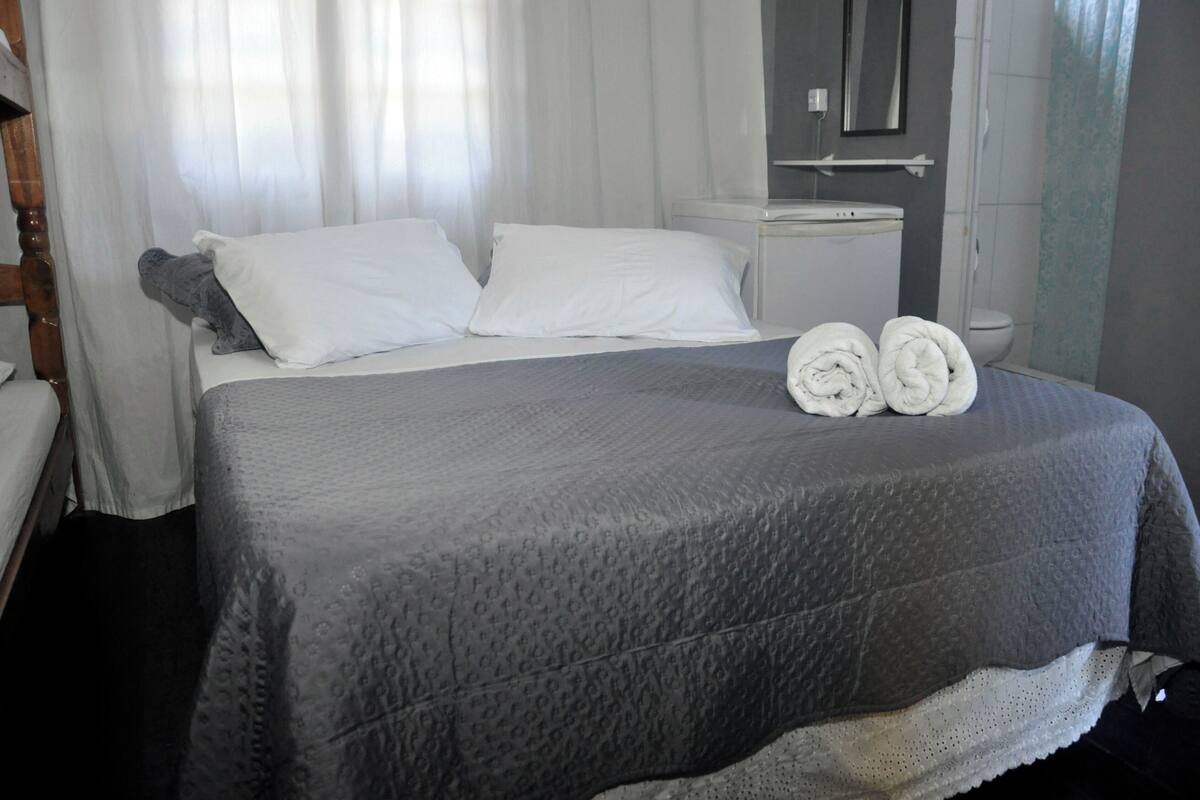 A bed with a grey quilt, two white pillows, and two rolled towels.