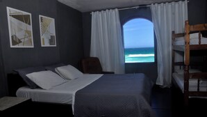 Een slaapkamer met een bed, een stoel, een stapelbed en een raam met uitzicht op de oceaan.