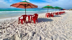 Een strand met rijen rode plastic stoelen en groene parasols, uitgestald op het zand.