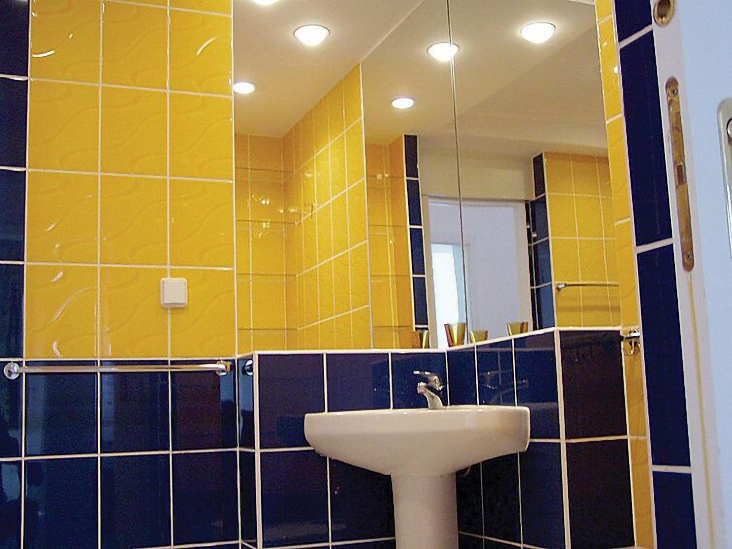 A bathroom with yellow and blue tiles, a white sink, and a mirror.