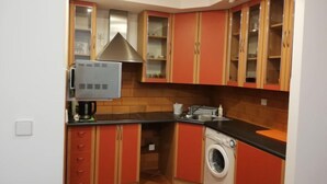 Cocina compacta con armarios rojos, microondas integrado y lavadora.