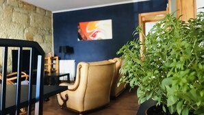 Ein Zimmer mit Steinwand, blauer Akzentwand, beigefarbenem Ohrensessel, schwarzem Sessel, Blumentopf und Deckenventilator.