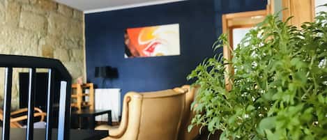 A room with a stone wall, a blue accent wall, a beige armchair, a black chair, a potted plant, and a ceiling fan.