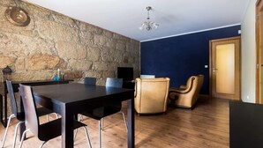 Ein Zimmer mit Steinwand, Holzboden, einem Esstisch mit Stühlen und einem Massagesessel sowie einer Tür.