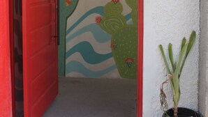 A red door leading into a room with a mural of cacti and waves.