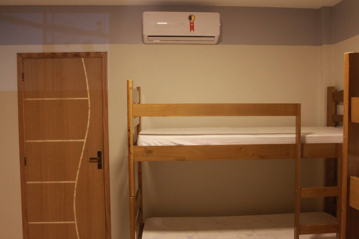 Dormitorio con literas, una puerta de madera y un equipo de aire acondicionado en la pared.