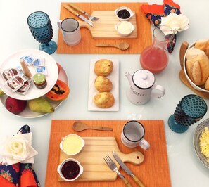 A breakfast setting with a plate of pastries, a pitcher of juice, and a cup of coffee on a table with orange placemats. - Massambaba Hostel (Arraial do Cabo)