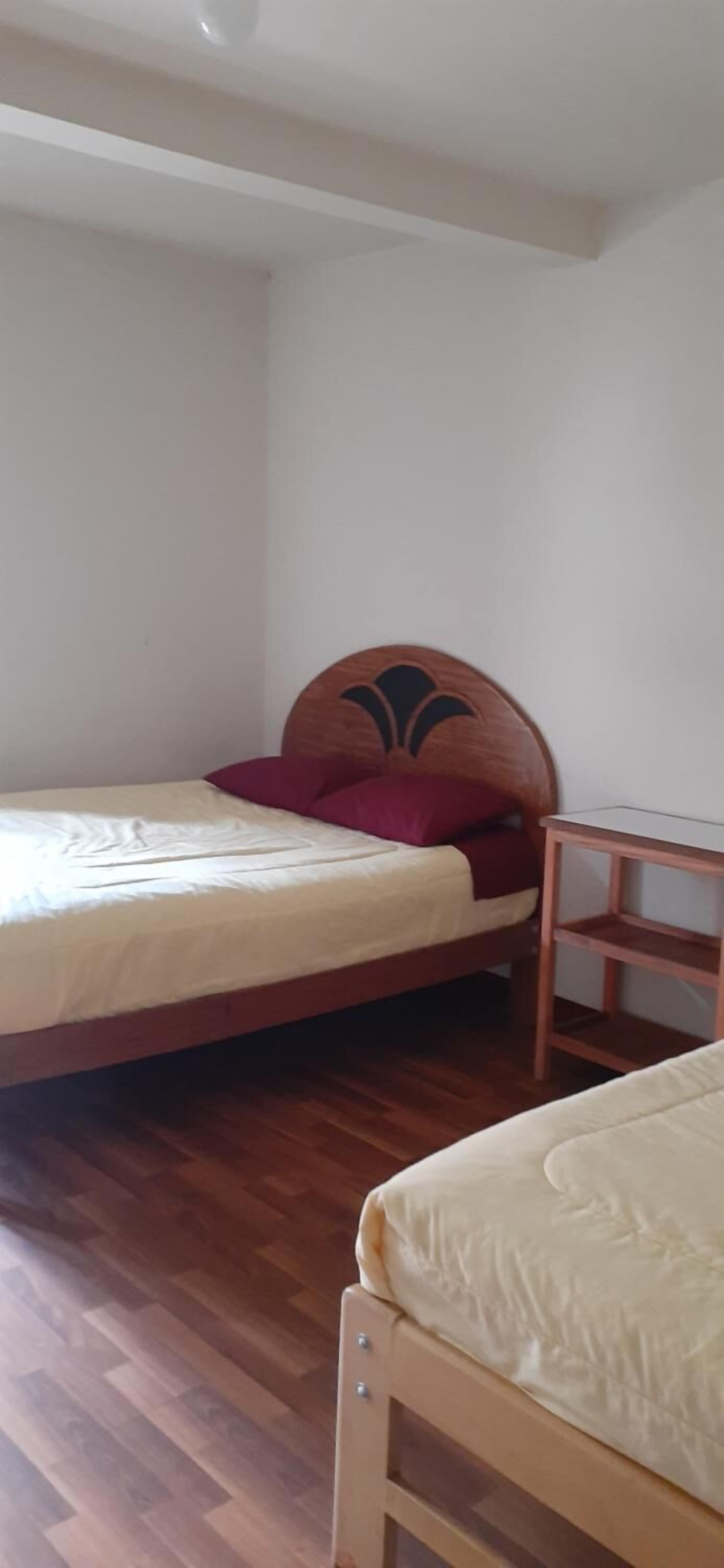 A small, simple room with two wooden beds, a wooden nightstand, and a white wall.