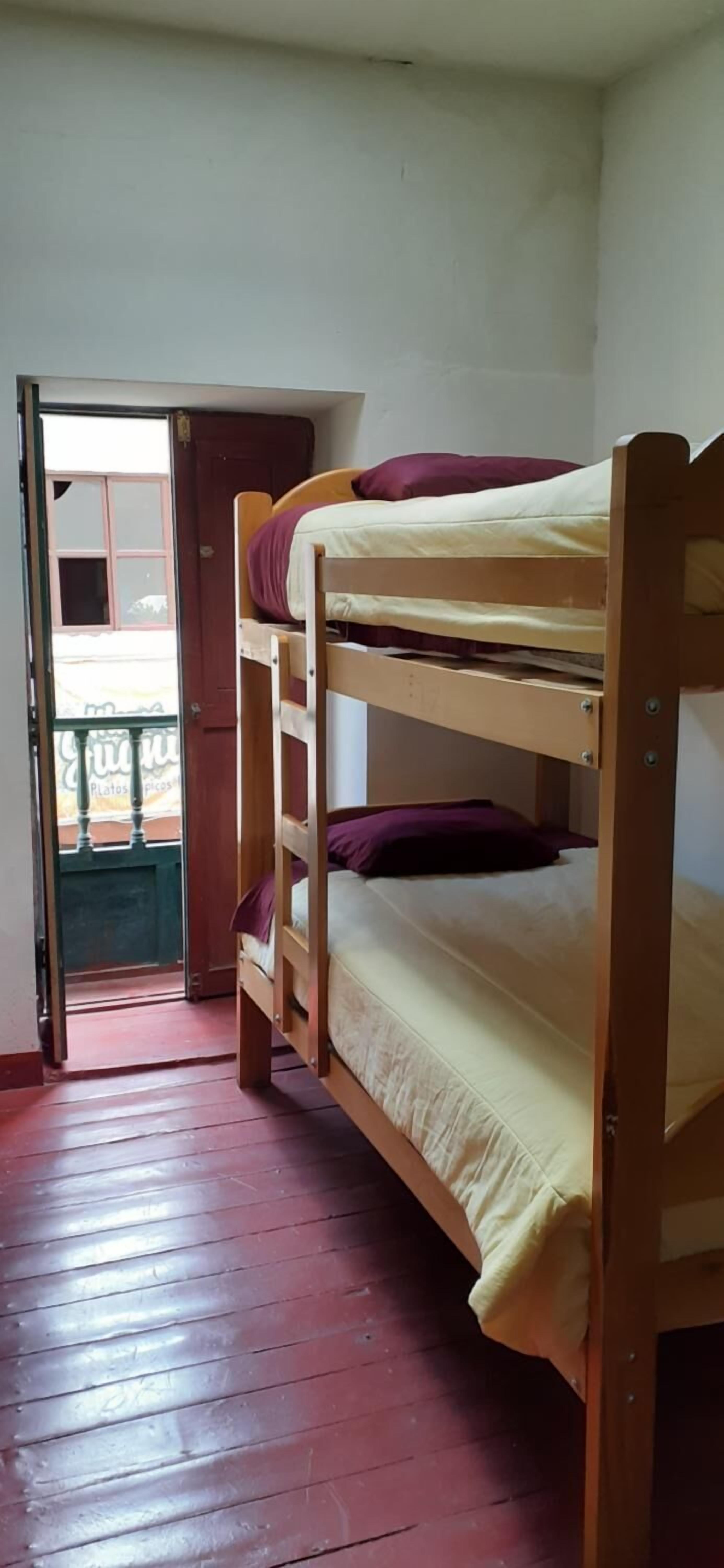 A bunk bed in a room with a wooden floor and a door leading to an outdoor area.