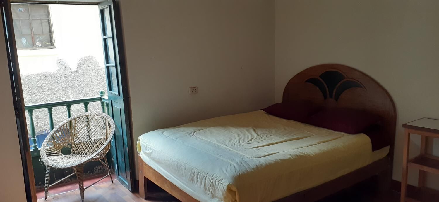Una habitació amb un llit, una cadira i un balcó.