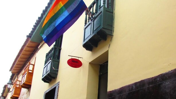 Un immeuble à la façade jaune, doté d’un balcon avec des balustrades vertes et d ’une enseigne circulaire rouge.