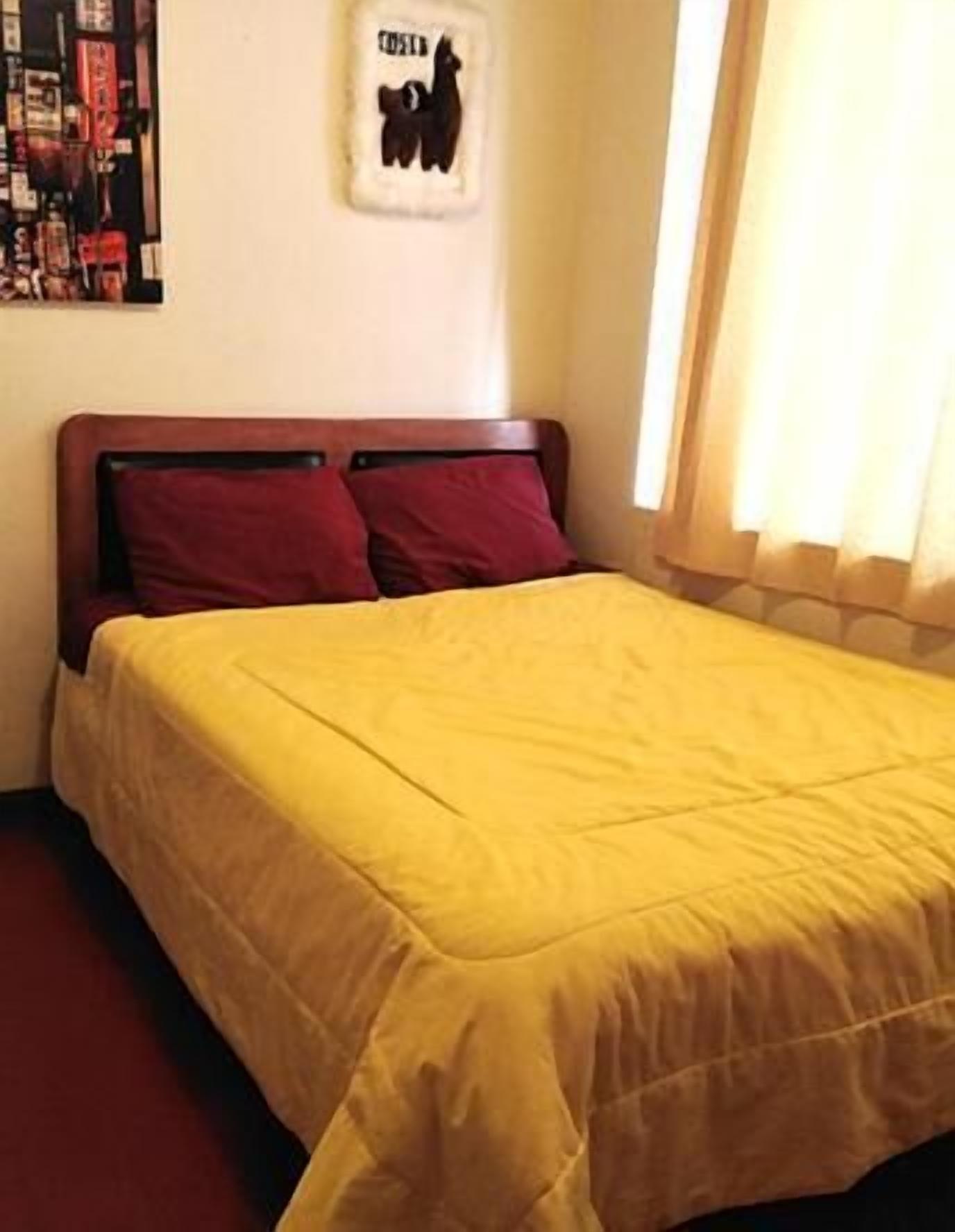 Una cama con colcha amarilla, dos almohadas rojas y un cabecero de madera.