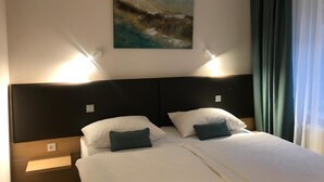 A hotel room with a large bed, two bedside tables, a wall-mounted painting, and a window with curtains.