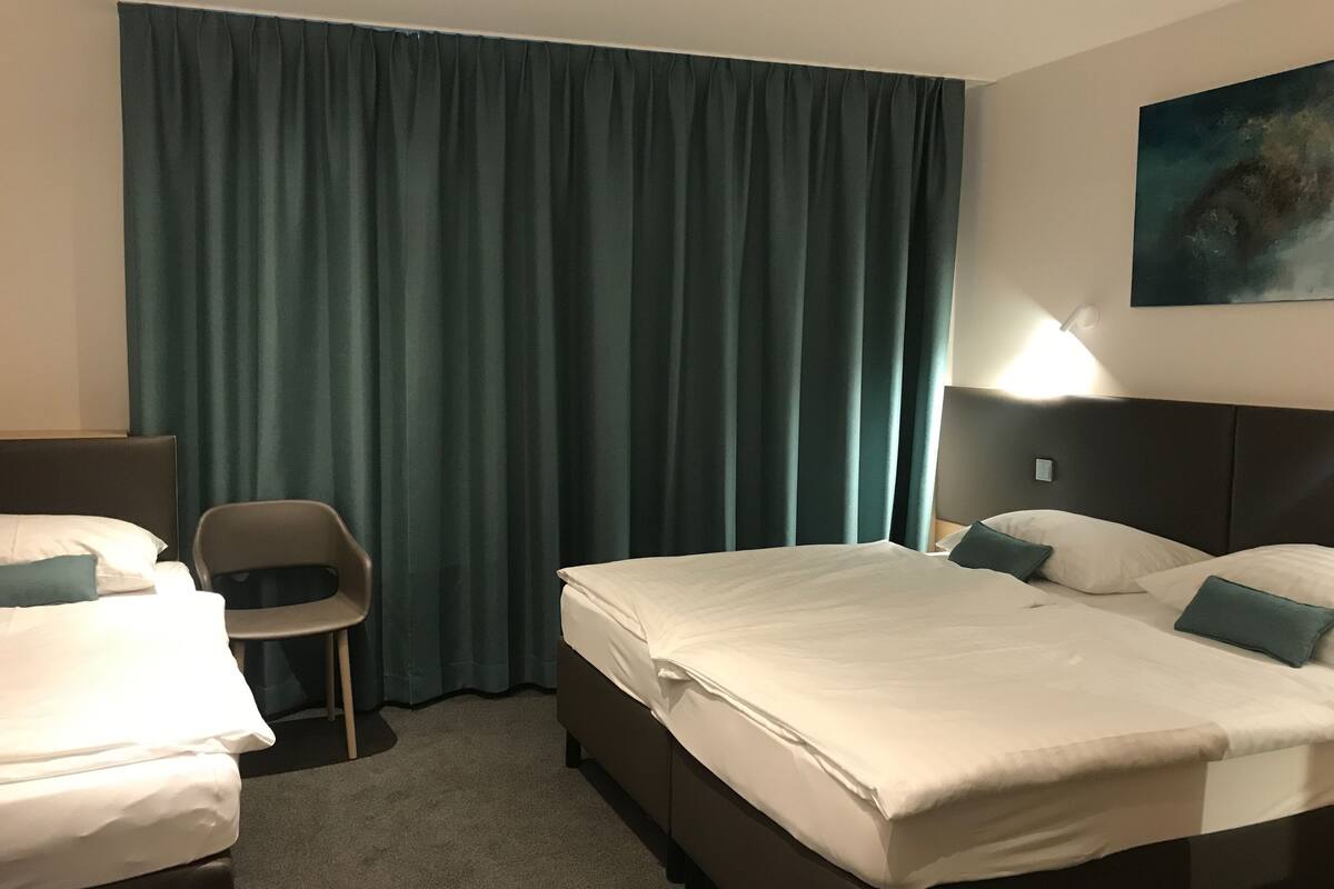 A hotel room with two beds, a chair, a desk, and a painting on the wall.