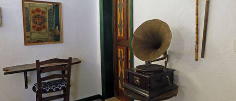 A room with a wooden chair, a gramophone, a patterned floor, a door, and a wall-mounted picture.