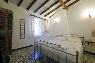 Una habitación con una cama bajo un dosel, una ventana con cortinas, una pared con un cuadro floral y un suelo estampado.