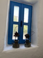 Una puerta azul con dos ventanas, una pared blanca y dos lámparas de aceite antiguas sobre el suelo.