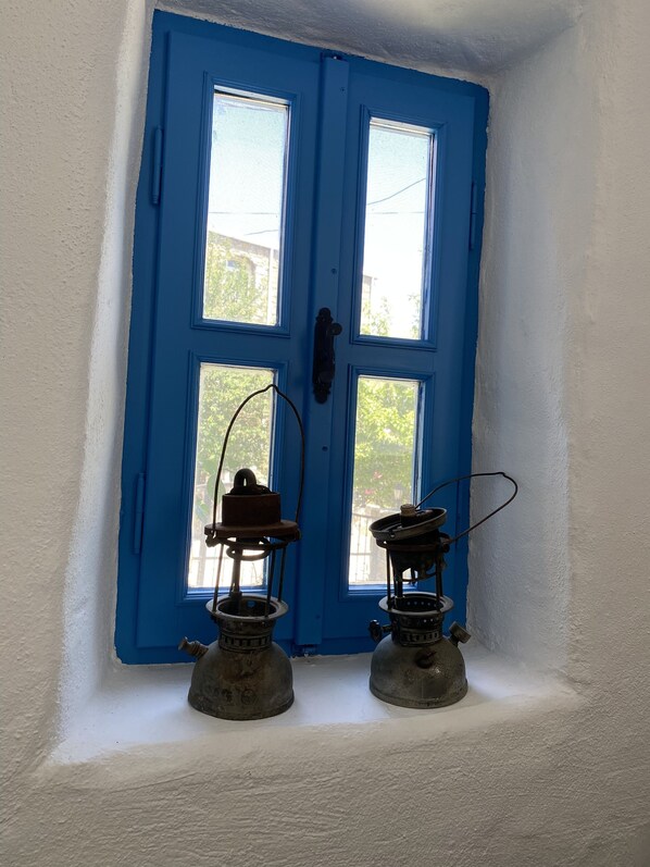 Une porte bleue avec deux fenêtres, un mur blanc et deux lampes à huile d’époque posées sur le sol.