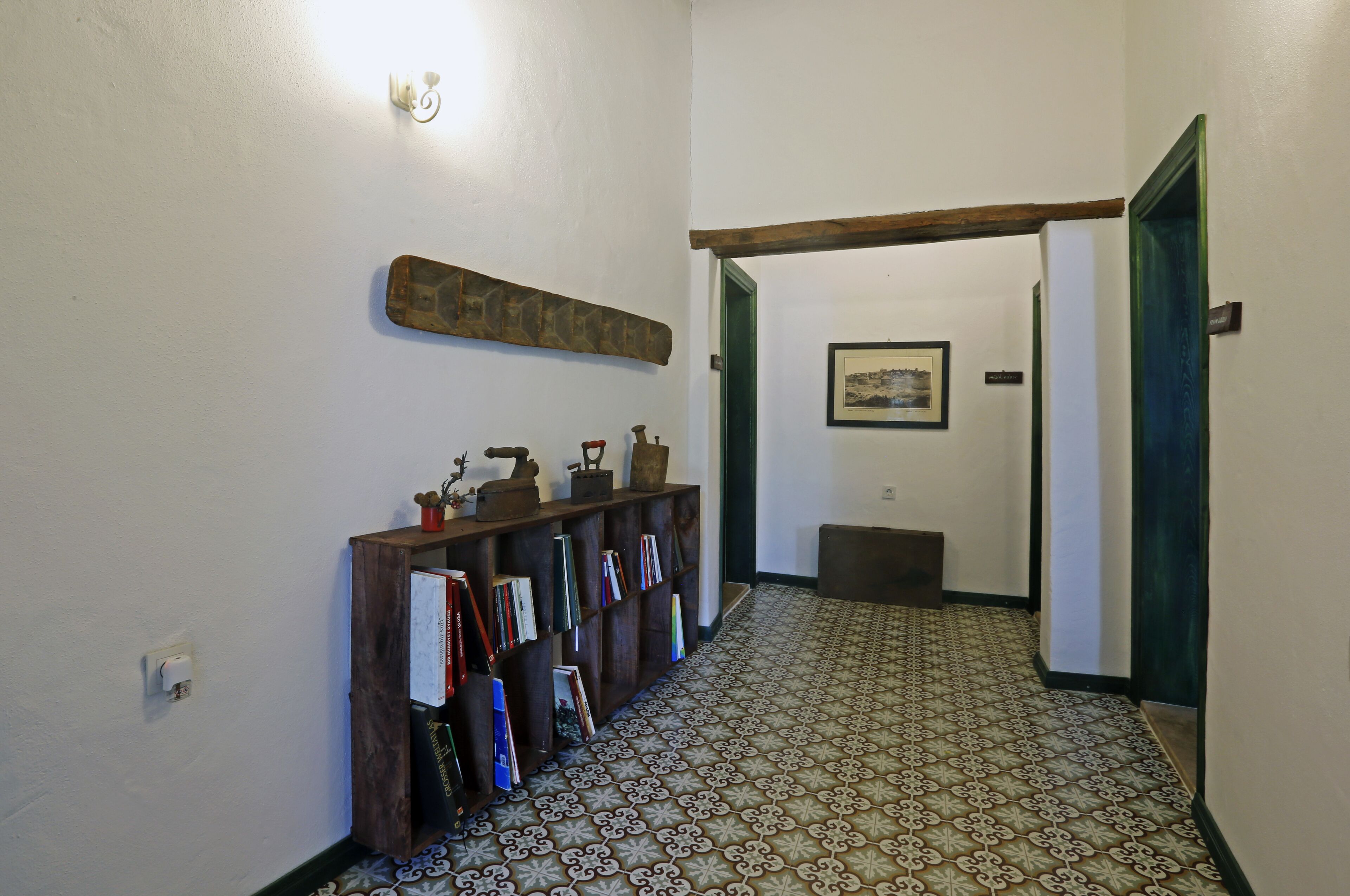 A hallway with patterned flooring, a wooden bookshelf with books, a wall-mounted light fixture, and a framed picture on the wall.