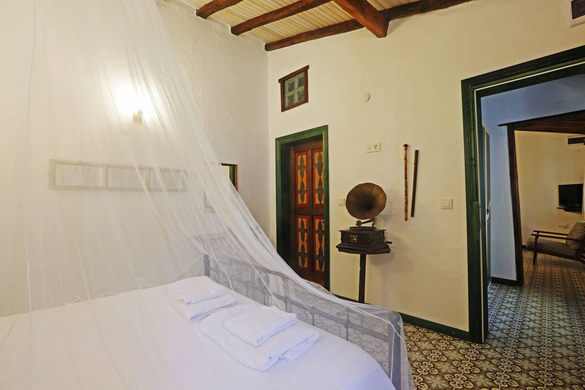 A room with a bed, a wooden door, a mirror, and a patterned floor.
