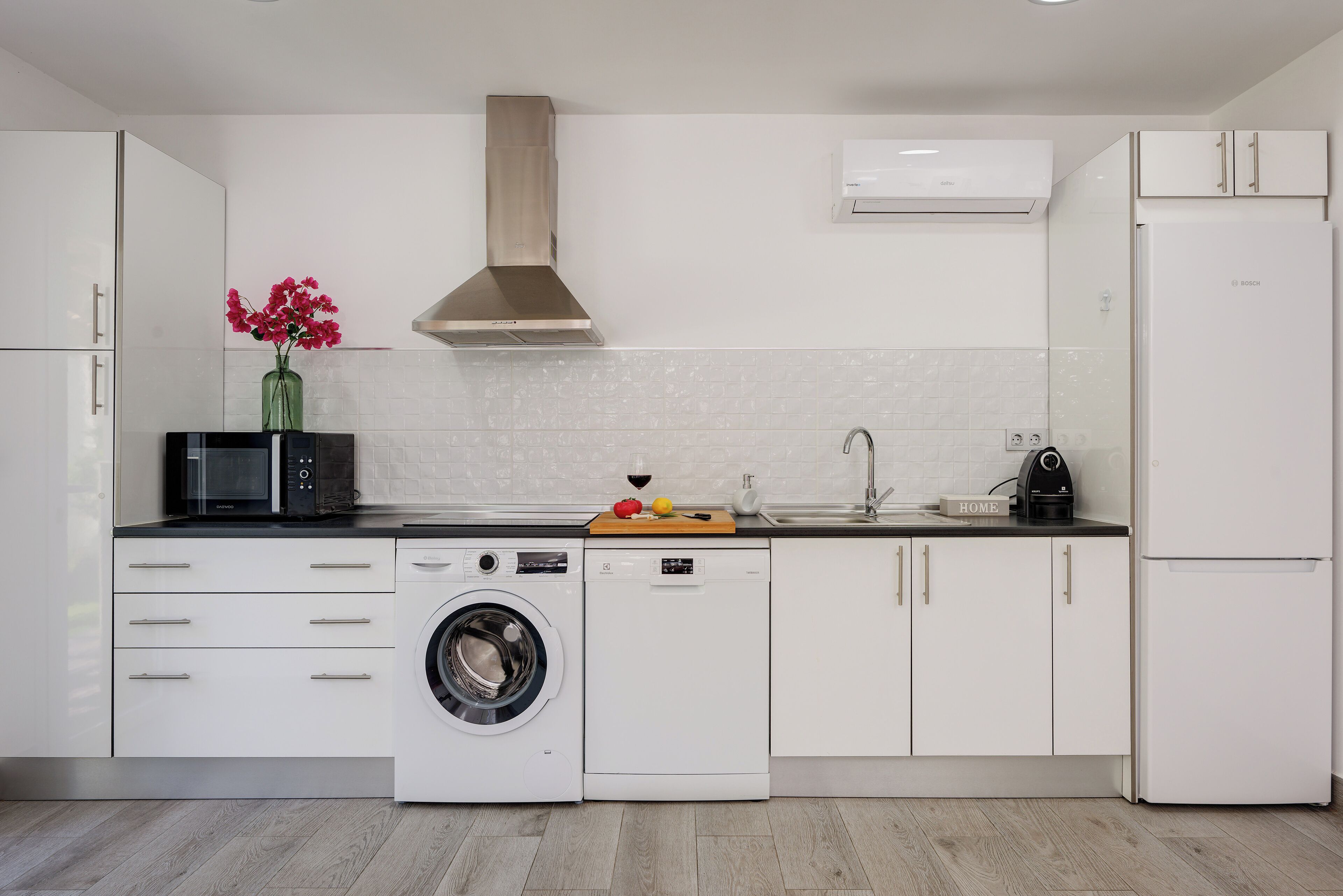 A modern kitchen with white cabinetry, a stainless steel range hood, a built-in washing machine, and a Bosch refrigerator.