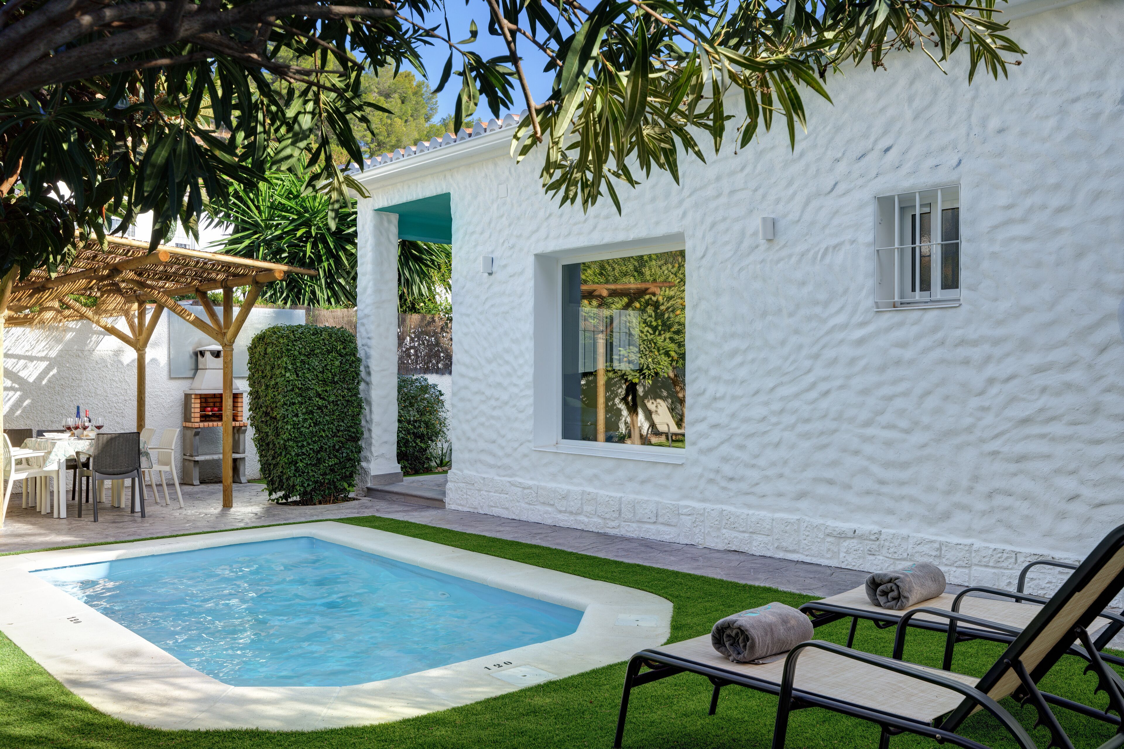 A white building with a swimming pool, outdoor seating, and a pergola.