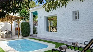 A white building with a swimming pool, outdoor seating, and a pergola.