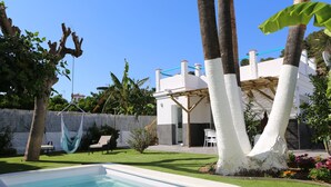 Ein Schwimmbad, eine Hängematte und ein weißes Gebäude mit einer überdachten Terrasse.