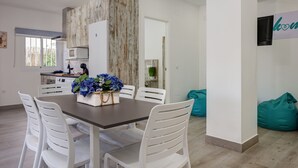 Eine moderne Küche mit weißen Schränken, einer Wand in Holzoptik und einem Essbereich mit weißen Stühlen und einem dunklen Tisch.