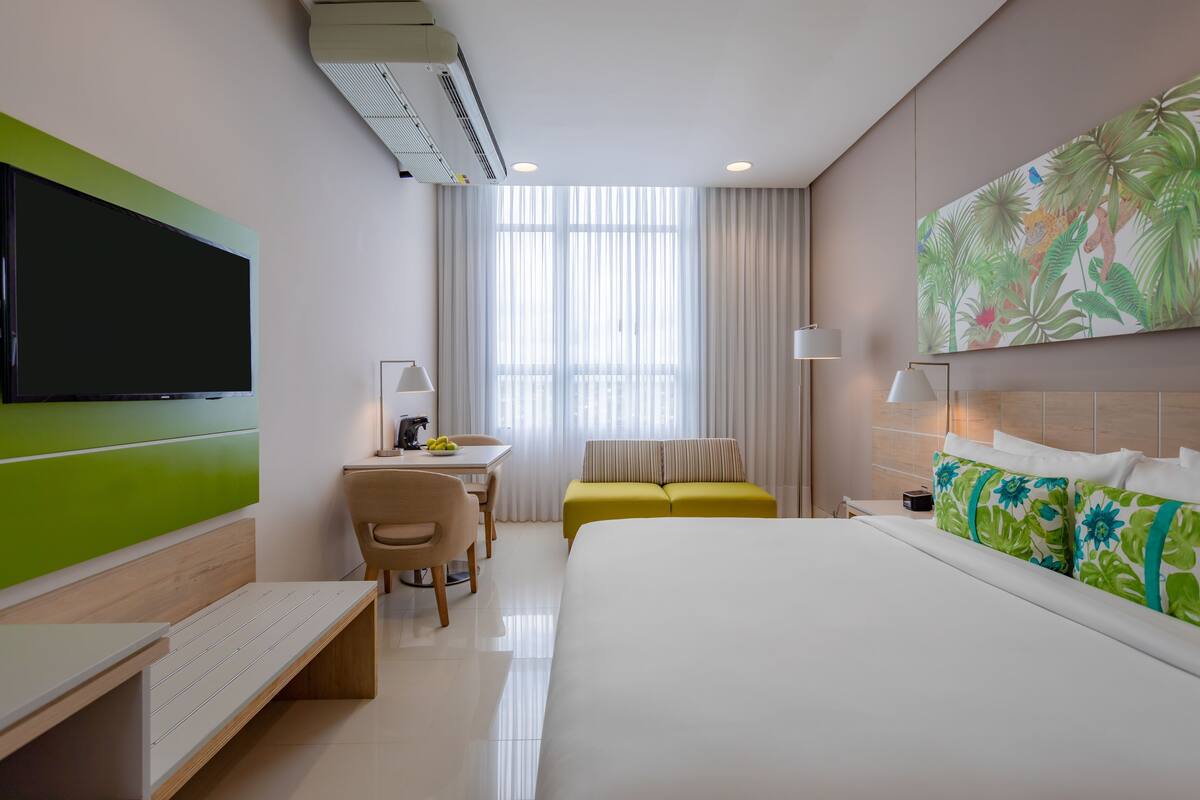 A hotel room with a bed, a desk, a chair, a television, and a large window with curtains.