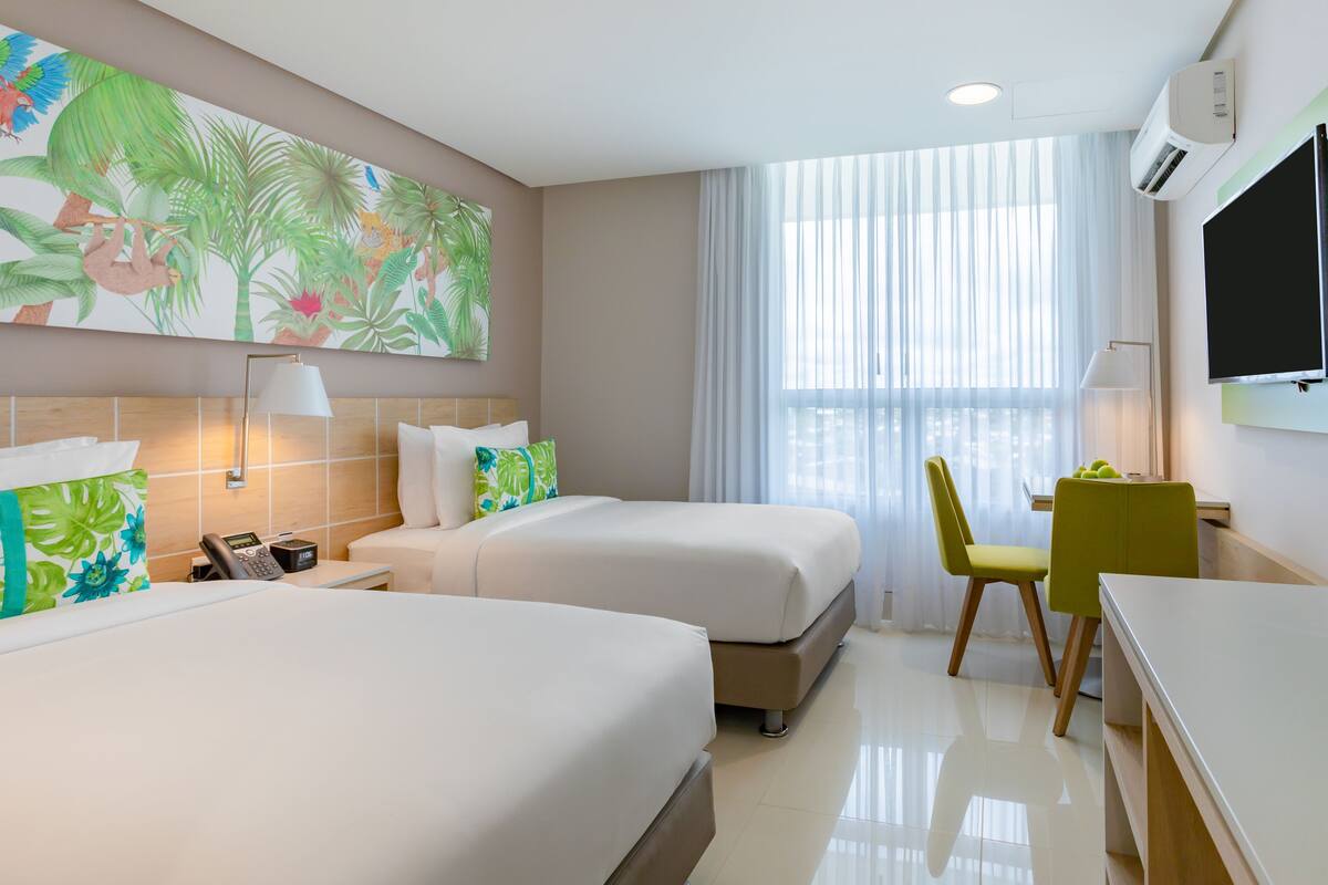 A hotel room with two beds, a desk, a chair, a TV, and a large window with curtains.