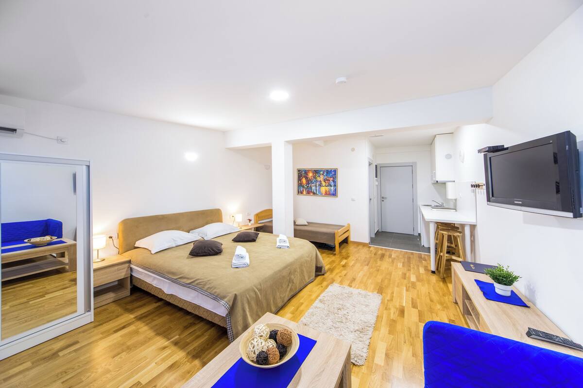 Quarto de hotel moderno com uma cama grande, mesas de cabeceira, escrivaninha, televisão e espelho.