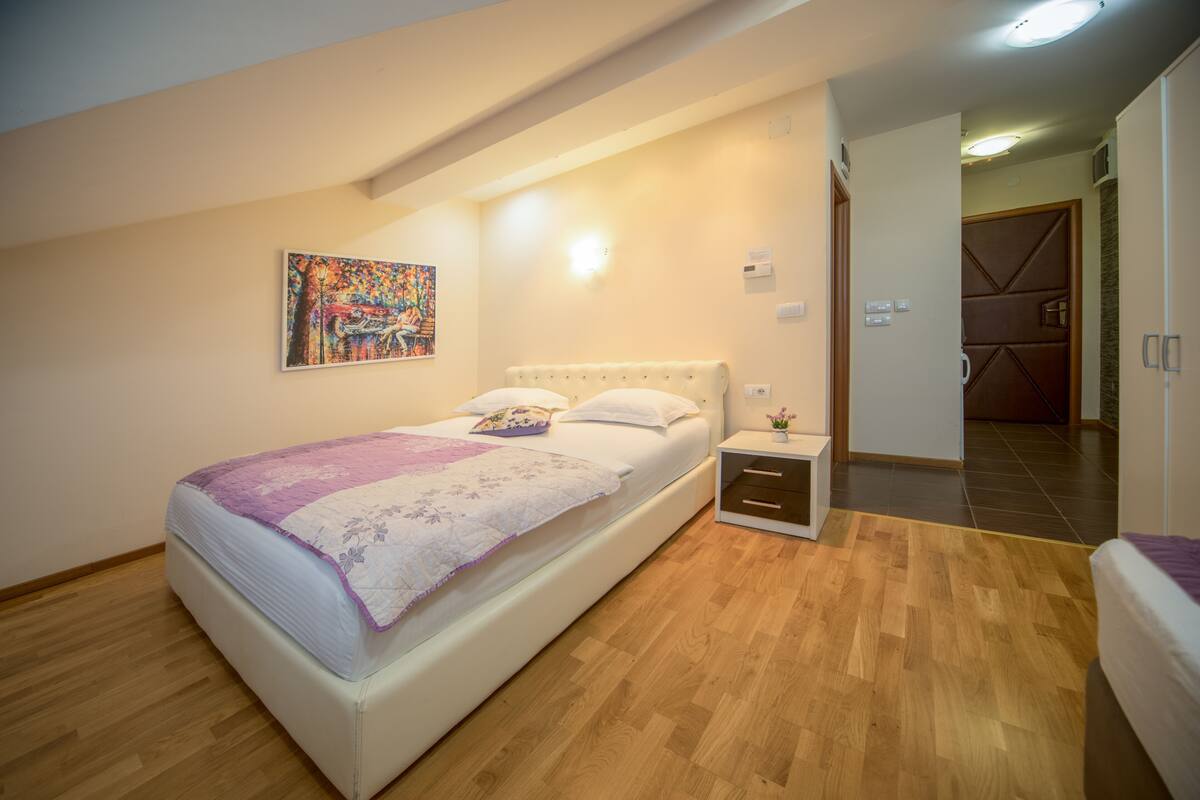 Quarto com cama, mesa de cabeceira, um quadro na parede e chão de madeira.