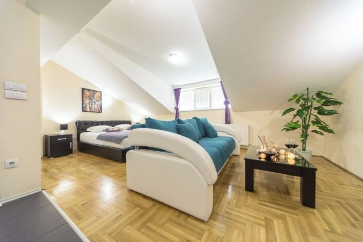 Un dormitorio con cama, sofá, mesita de noche, una mesa con objetos y una planta en maceta.